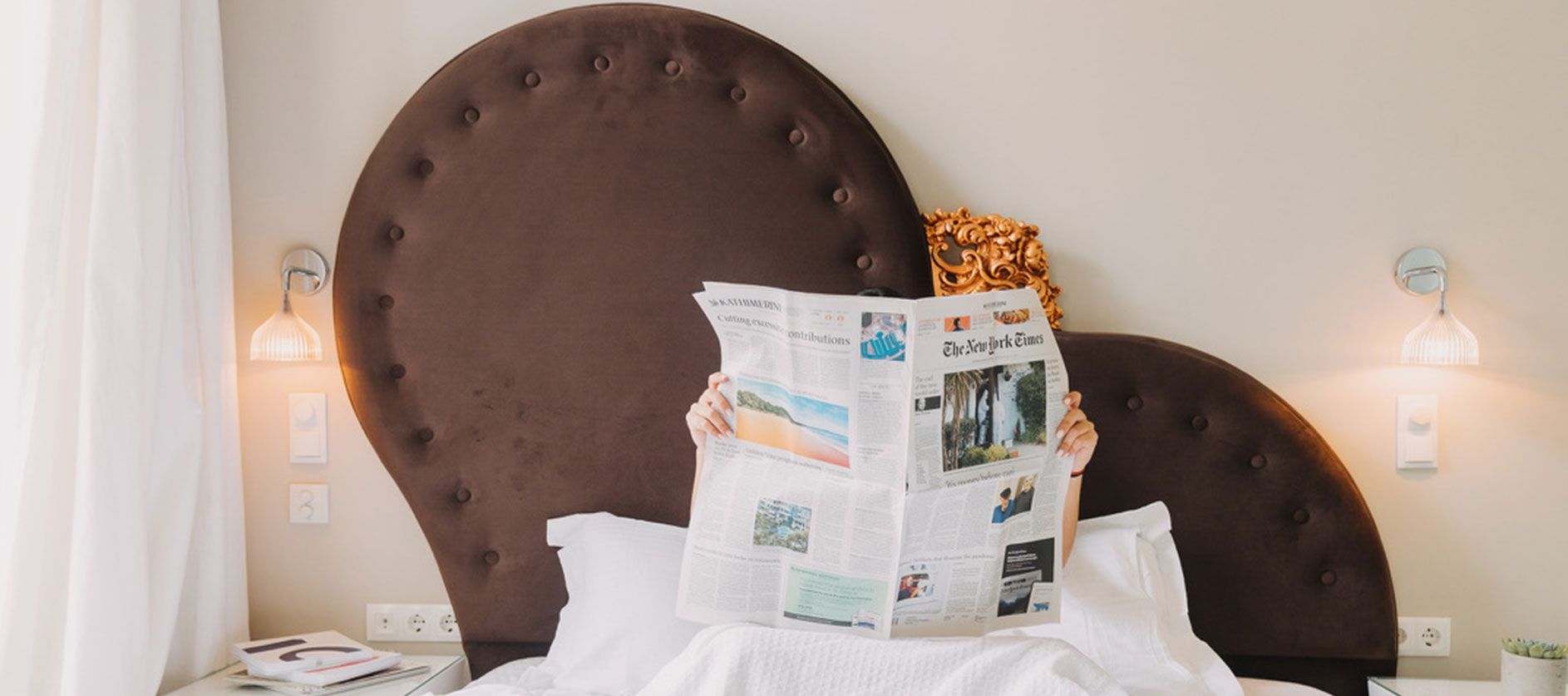 Guest reading the newspaper in bed under a heart shaped headboard