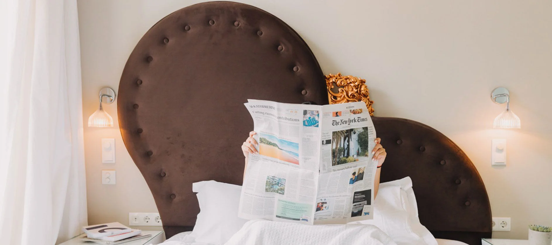 Guest reading the newspaper in bed under a heart shaped headboard